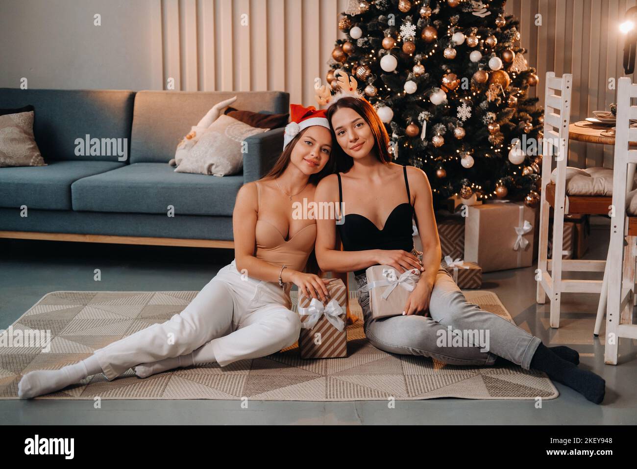 Zwei schöne junge Mädchen mit Weihnachtsgeschenken in den Händen sitzen in der Nähe des Weihnachtsbaums im Jahr house.friends mit Weihnachtskleider und Stockfoto