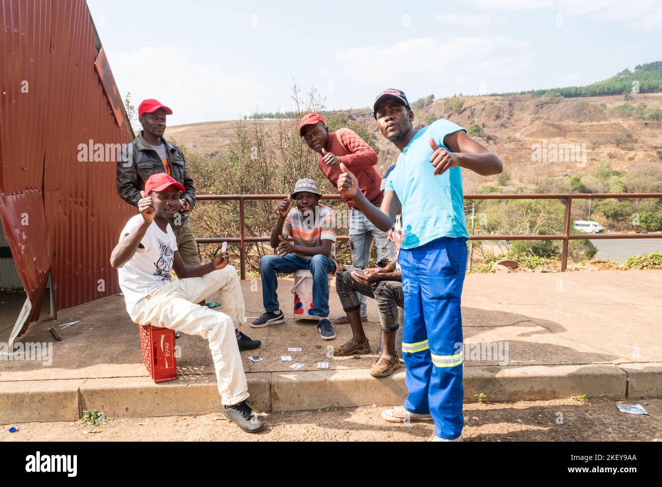 Südafrikanische Gruppe von Männern spielen ein Kartenspiel auf der Seite der Straße geben einen freundlichen Gruß oder Daumen nach oben Konzept des täglichen Lebens in Afrika Stockfoto