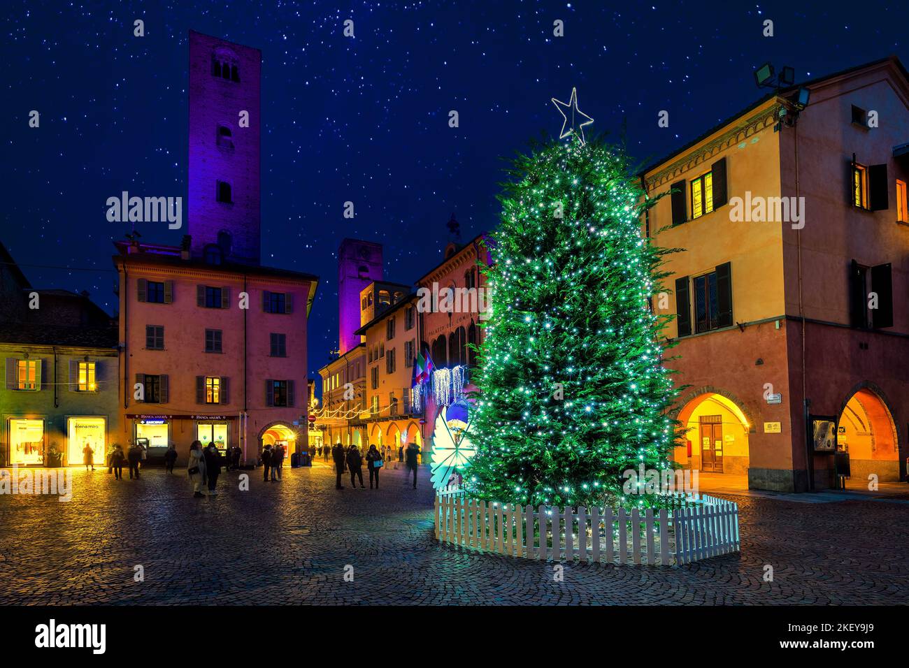 Menschen, die auf den beleuchteten Weihnachtsbaum auf dem Stadtplatz zwischen dem alten historischen Gebäude in Alba, Italien, schauen. Stockfoto