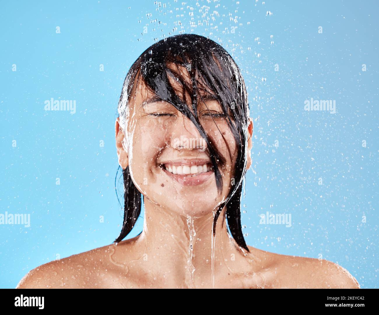 Dusche, Frau und Wasser mit Gesichtsreinigung für Reinigung, Reinigung und Hygiene auf blauem Studiohintergrund. Bad, Dusche und asiatische weibliche Reinigung Stockfoto