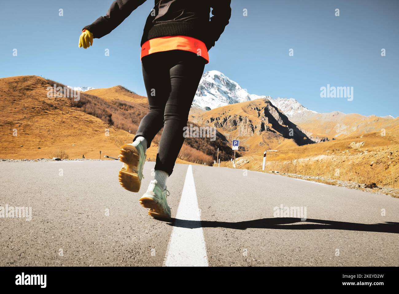 Rückansicht Frau Nahaufnahme auf der Straße Lauf mit bequemen Wandern Universalschuhe mit Gummimatte auf der Straße mit malerischen Bergen Hintergrund. Kazbegi-Nationalmannschaft Stockfoto