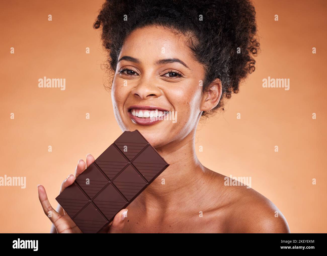 Schokolade, glückliche Frau und Schönheitsporträt auf Studiohintergrund beim Essen von Süßigkeiten, Dessert oder Zucker. Junge afroamerikanische Mädchen beißen dunkle Schokolade Bar Stockfoto