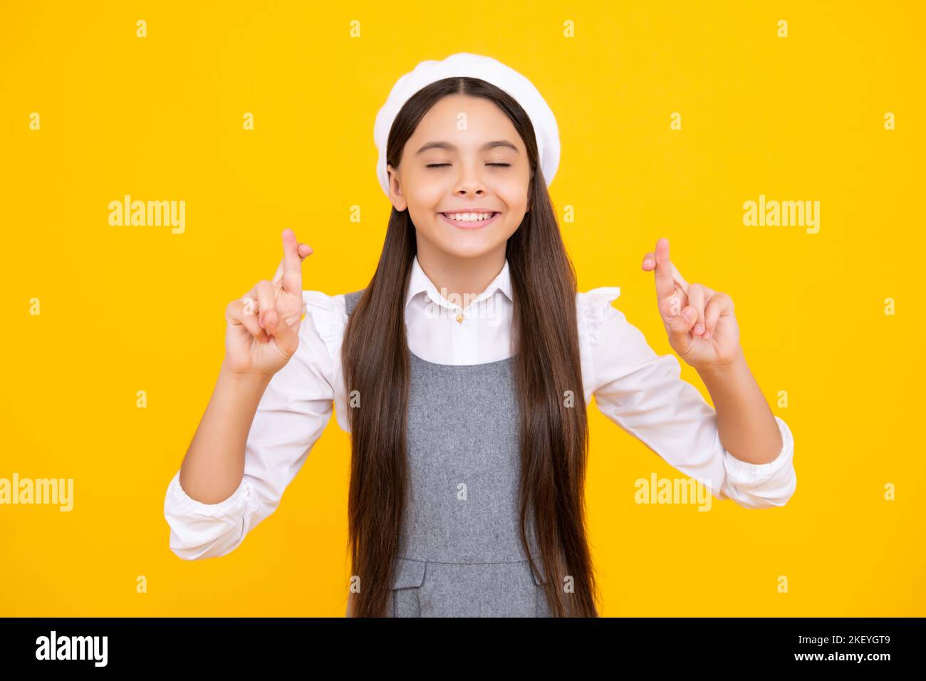 Zufrieden fröhlich Teenager Kind wünscht viel Glück, kreuzt die Finger, hat Vertrauen für besser, isoliert über gelben Hintergrund. Stockfoto