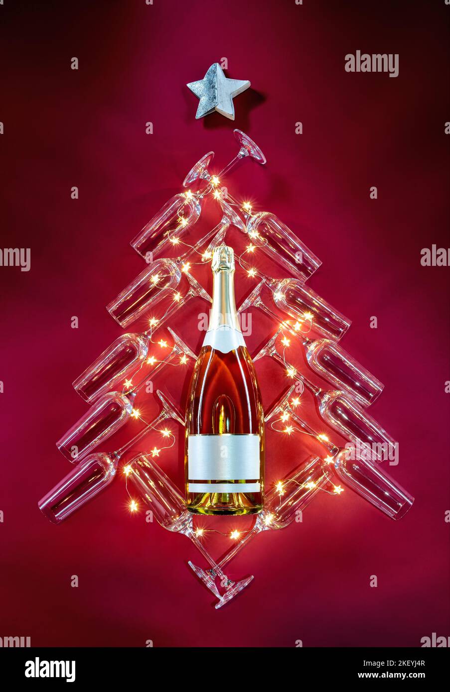 Silhouette eines festlichen Baumes, eine Flasche Champagner, umgeben von Gläsern und Sternen auf rotem Hintergrund. Frohe Weihnachten und ein glückliches neues Jahr Konzept Stockfoto