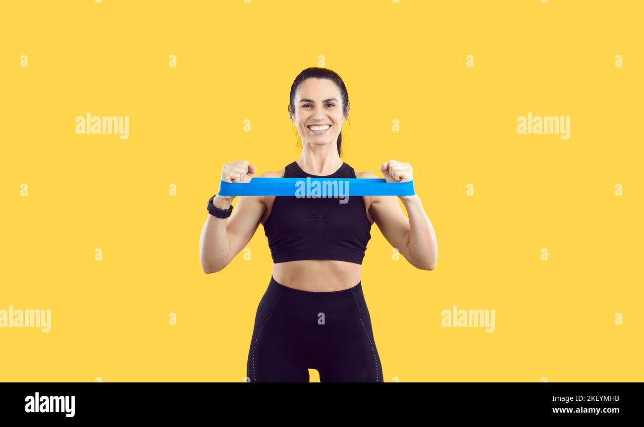 Sportlerin auf gelbem Hintergrund mit ihren Händen dehnt Gummiband für das Training. Stockfoto