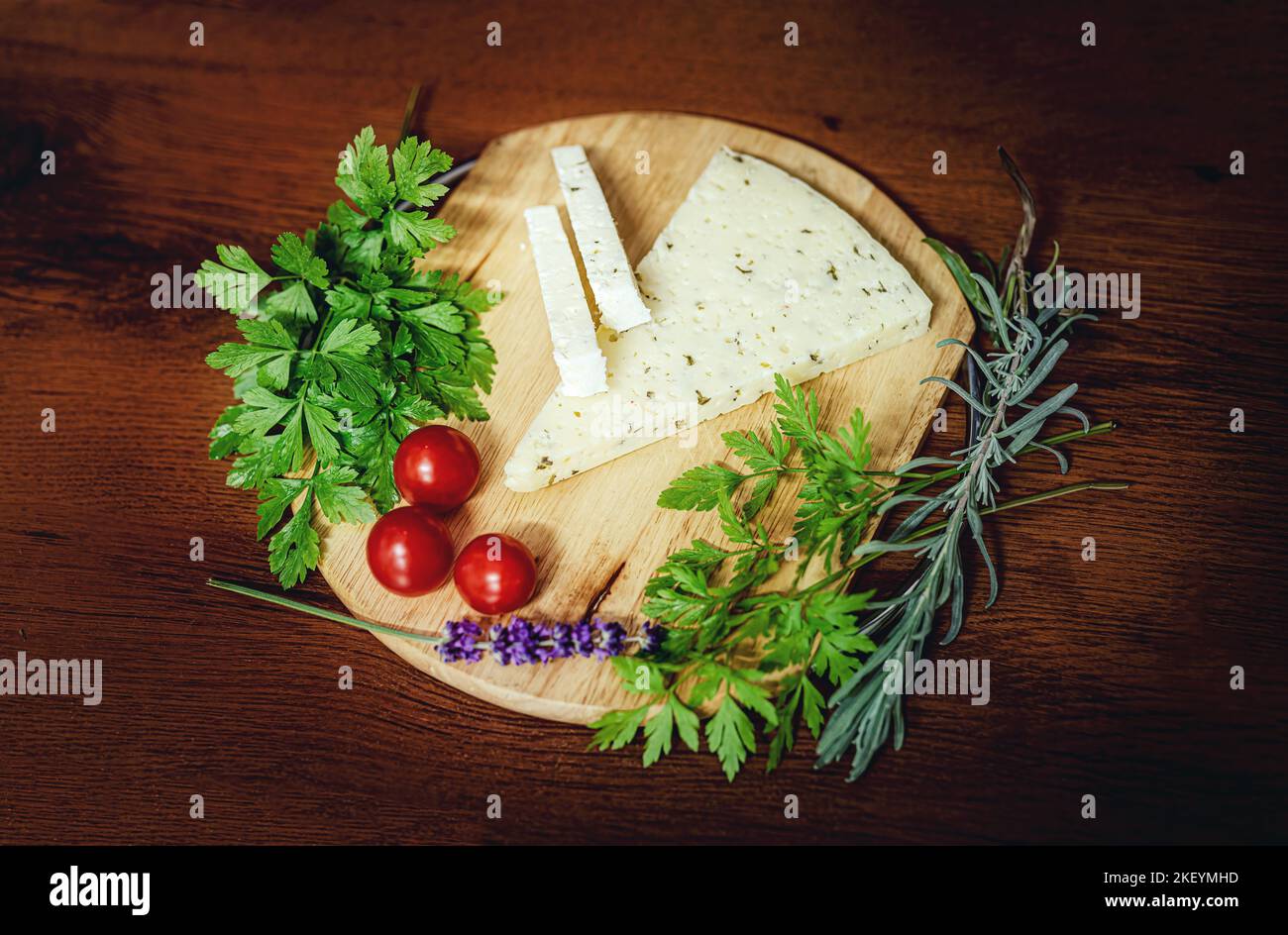 Handgefertigter ländlicher Käse auf einem Holzbrett mit Gemüsedekoration auf Wiesenhintergrund. Stockfoto