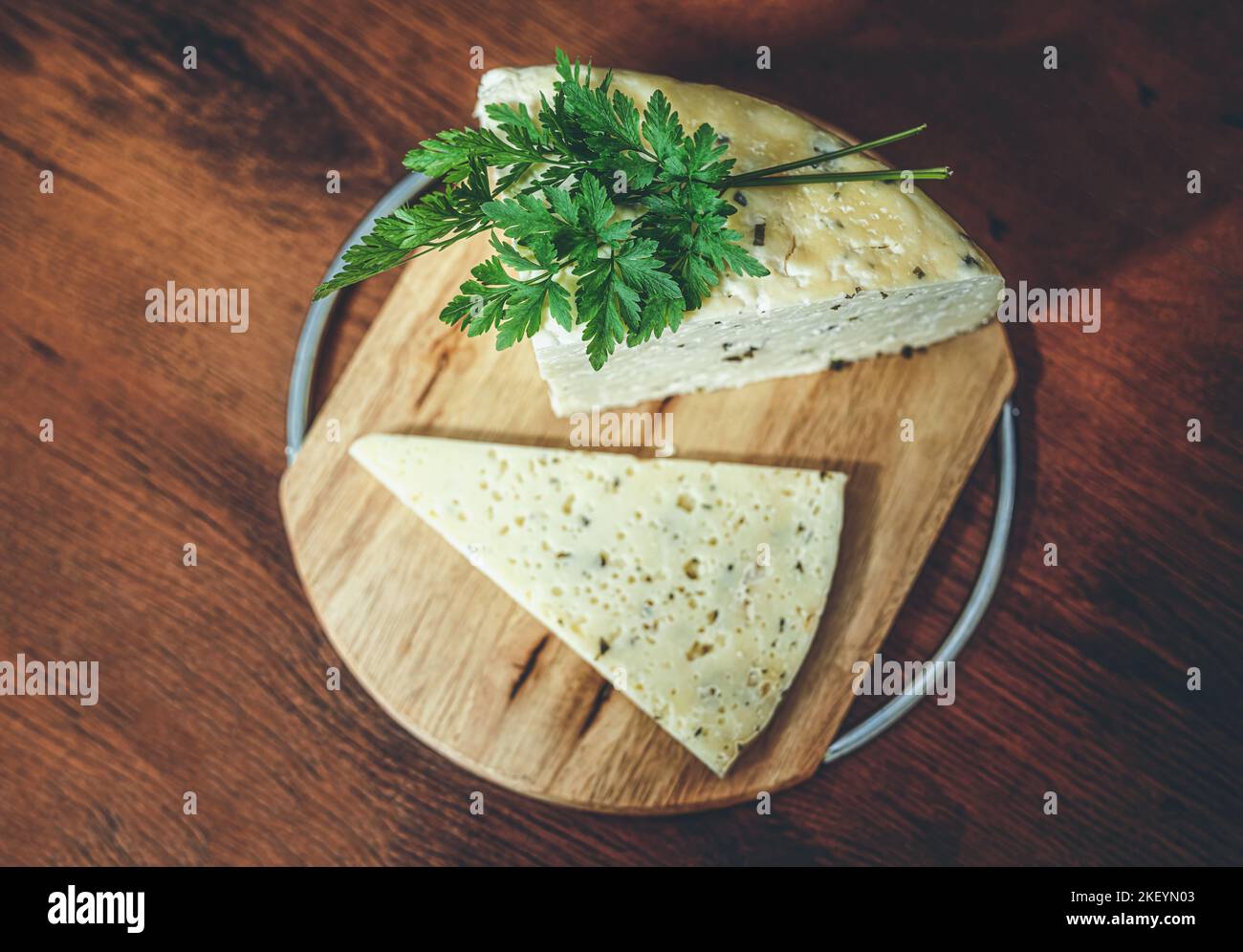 Handgefertigter ländlicher Käse auf einem Holzbrett mit Gemüsedekoration auf Wiesenhintergrund. Stockfoto