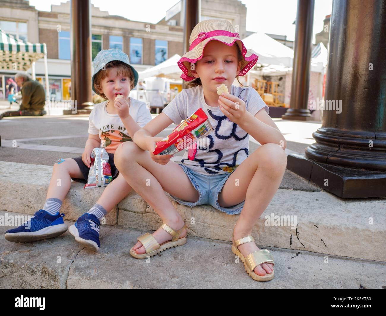 Kleine Kinder, ein Junge und ein Mädchen, die draußen auf dem Boden Snacks essen Stockfoto