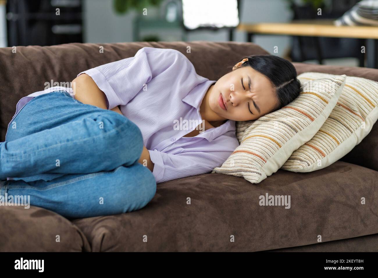 Frau mit Bauchschmerzen, die zu Hause auf der Couch liegt Frau mit starken Krämpfen, die ihren Magen halten Stockfoto