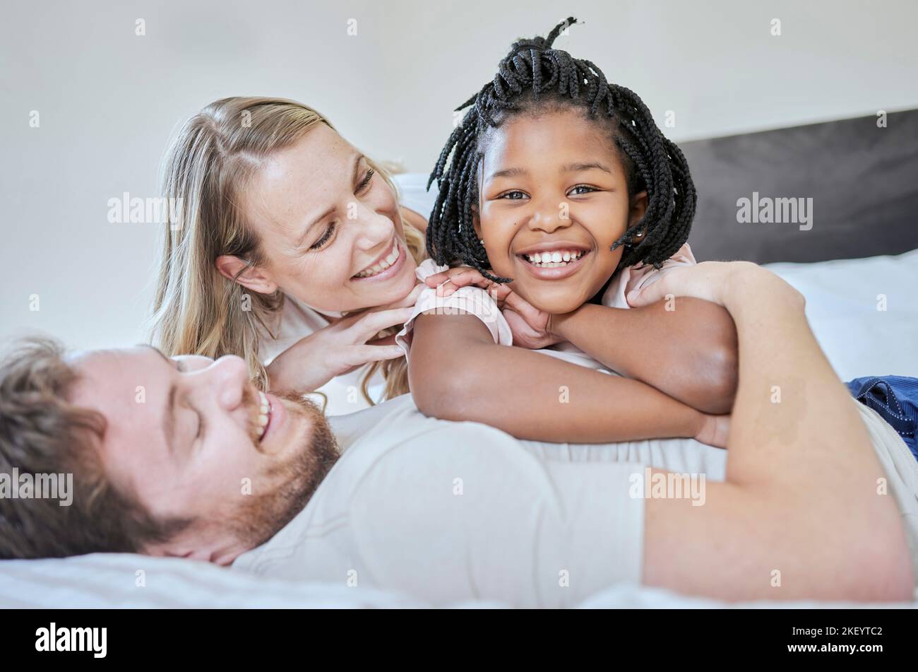 Liebe, Adoption und Familienportrait, entspannen und lächeln auf dem Bett zu Hause, glücklich und Unterstützung mit Sorgfalt. Mutter, Vater und schwarzes Mädchen, Glück und Freiheit Stockfoto