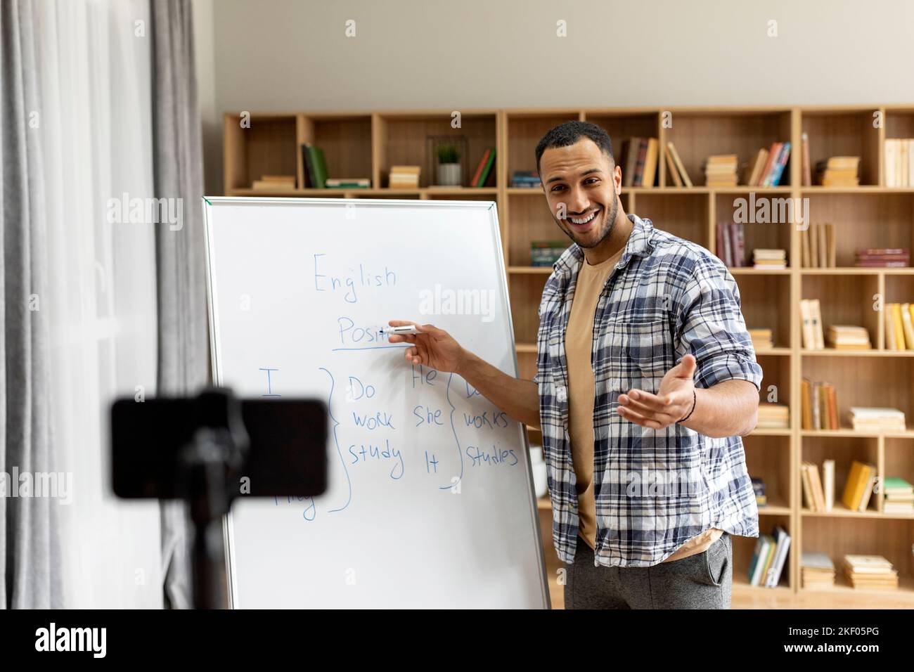 Virtueller Unterricht, Unterricht und Training, Studium zu Hause. Glücklicher männlicher Lehrer, der auf das Whiteboard zeigt und vor der Webcam des Telefons spricht Stockfoto