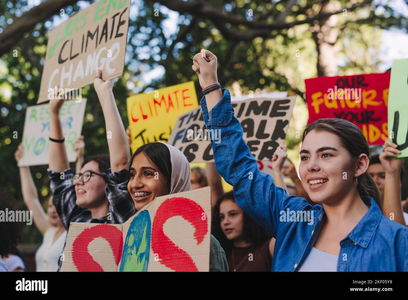 Fröhliche Jugendaktivisten erheben ihre Fäuste gegen den Klimawandel und die globale Erwärmung. Eine Gruppe verschiedener junger Menschen protestierte mit Plakaten und Spruchbändern Stockfoto