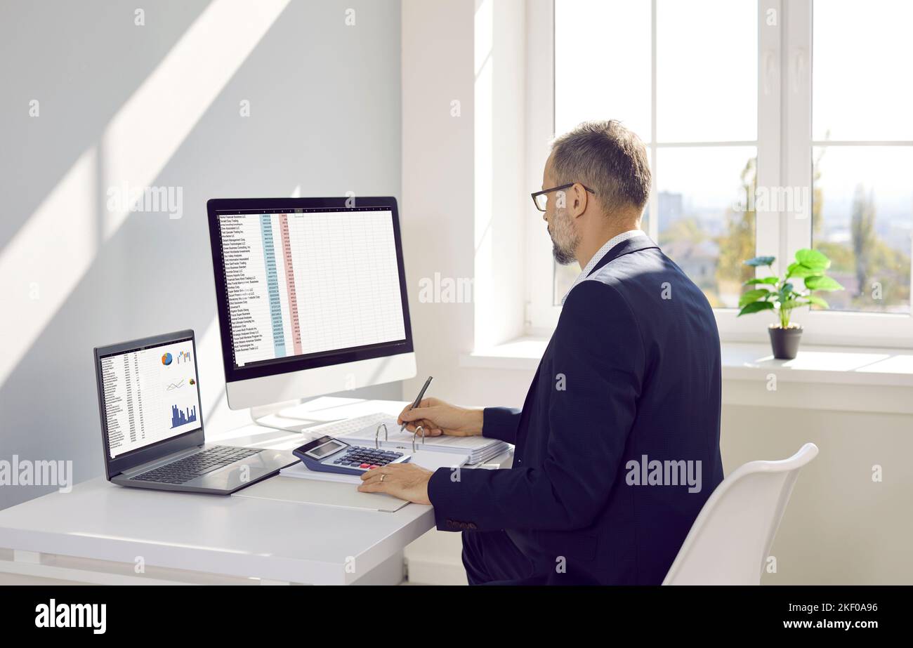 Wirtschaftsprüfer, der am Schreibtisch sitzt und an Desktop- und Laptop-Computern arbeitet Stockfoto