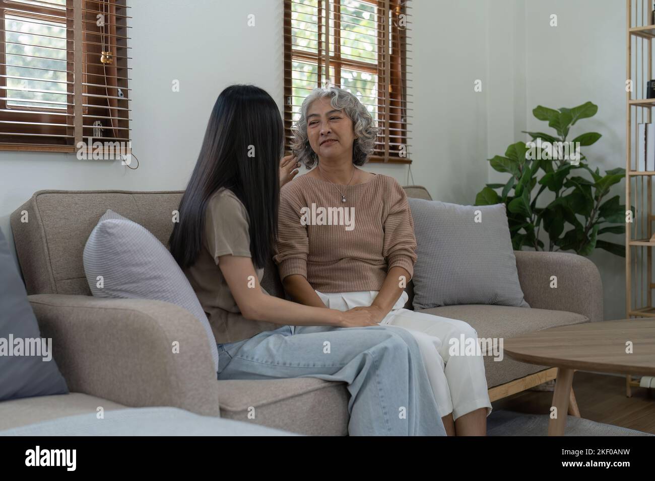 Liebevolle Erwachsene Tochter umarmt ältere Mutter auf der Couch zu Hause, Familie genießen zarten Moment zusammen, junge Frau und reife Mutter oder Großmutter suchen Stockfoto