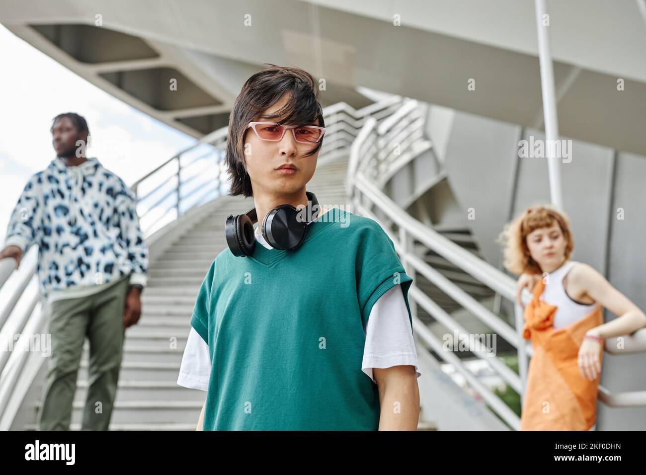 Eine vielfältige Gruppe junger Menschen, die Straßenkleidung im Freien tragen, konzentriert sich auf asiatische Männer mit Kopfhörern im Vordergrund Stockfoto