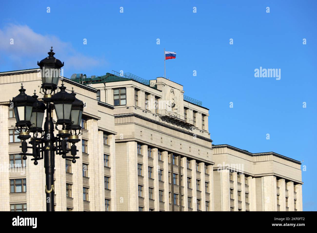 Parlamentsgebäude in Moskau mit russischer Flagge auf dem Hintergrund des blauen Himmels. Fassade der russischen Staatsduma mit sowjetischem Wappen, russische Autorität Stockfoto