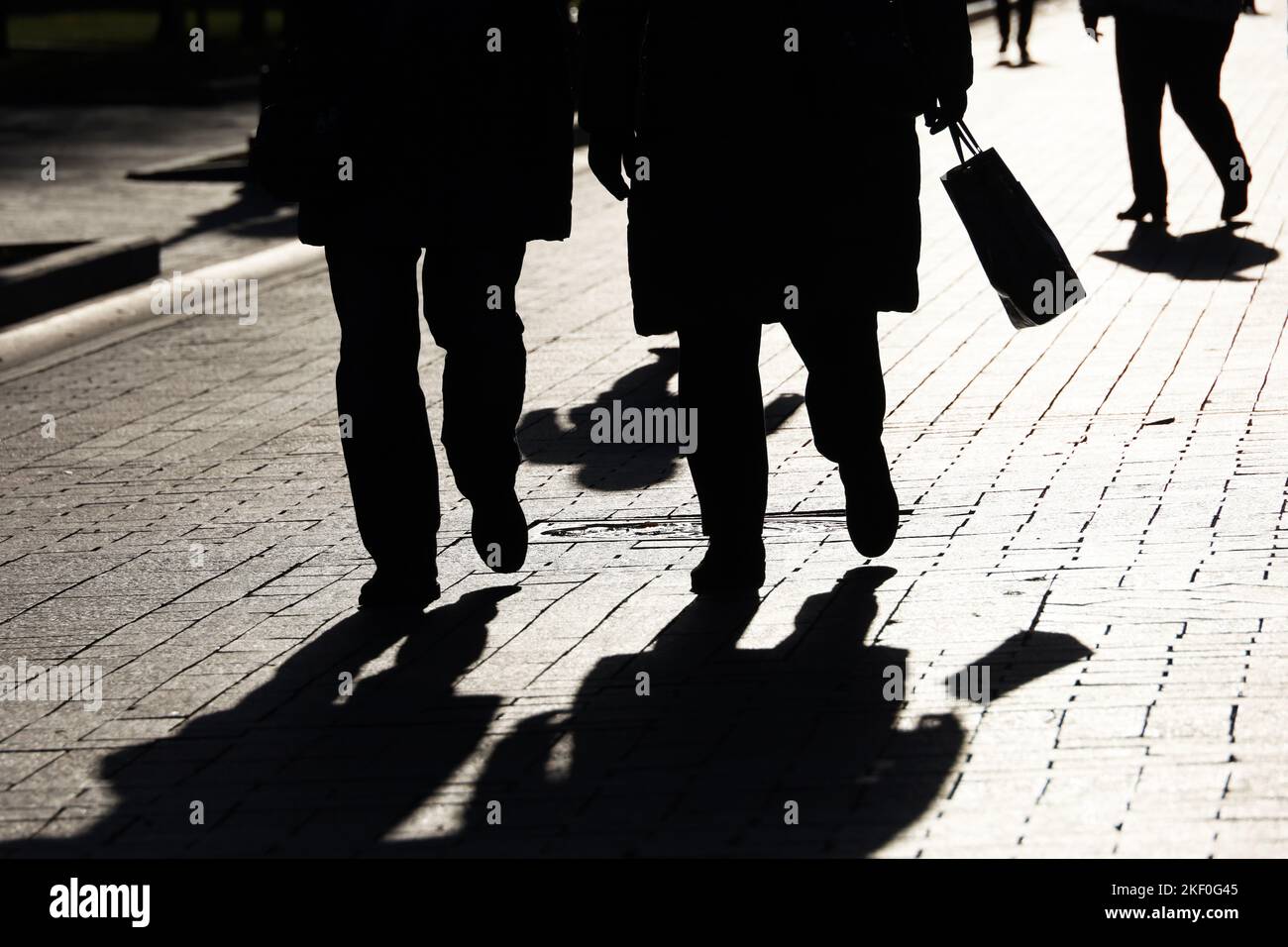 Silhouetten und Schatten von Menschen auf der Stadtstraße. Zwei Frauen im Vordergrund, die auf dem Bürgersteig nach unten gehen, Konzept von Gesellschaft und Bevölkerung Stockfoto