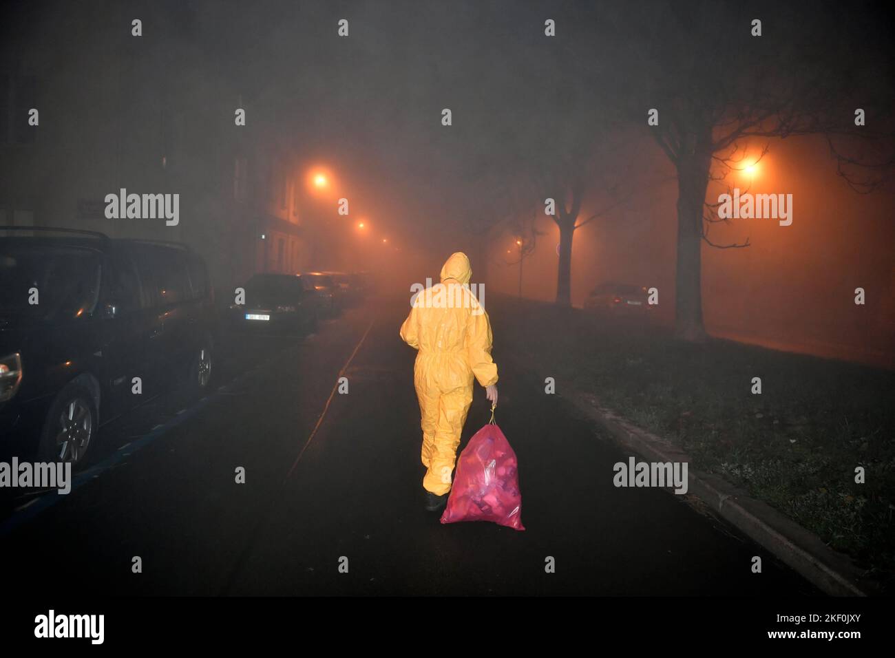 Eine Person in gelber Farbe, die auf der nächtlichen, rauchigen Straße mit einem Müllsack unterwegs ist Stockfoto