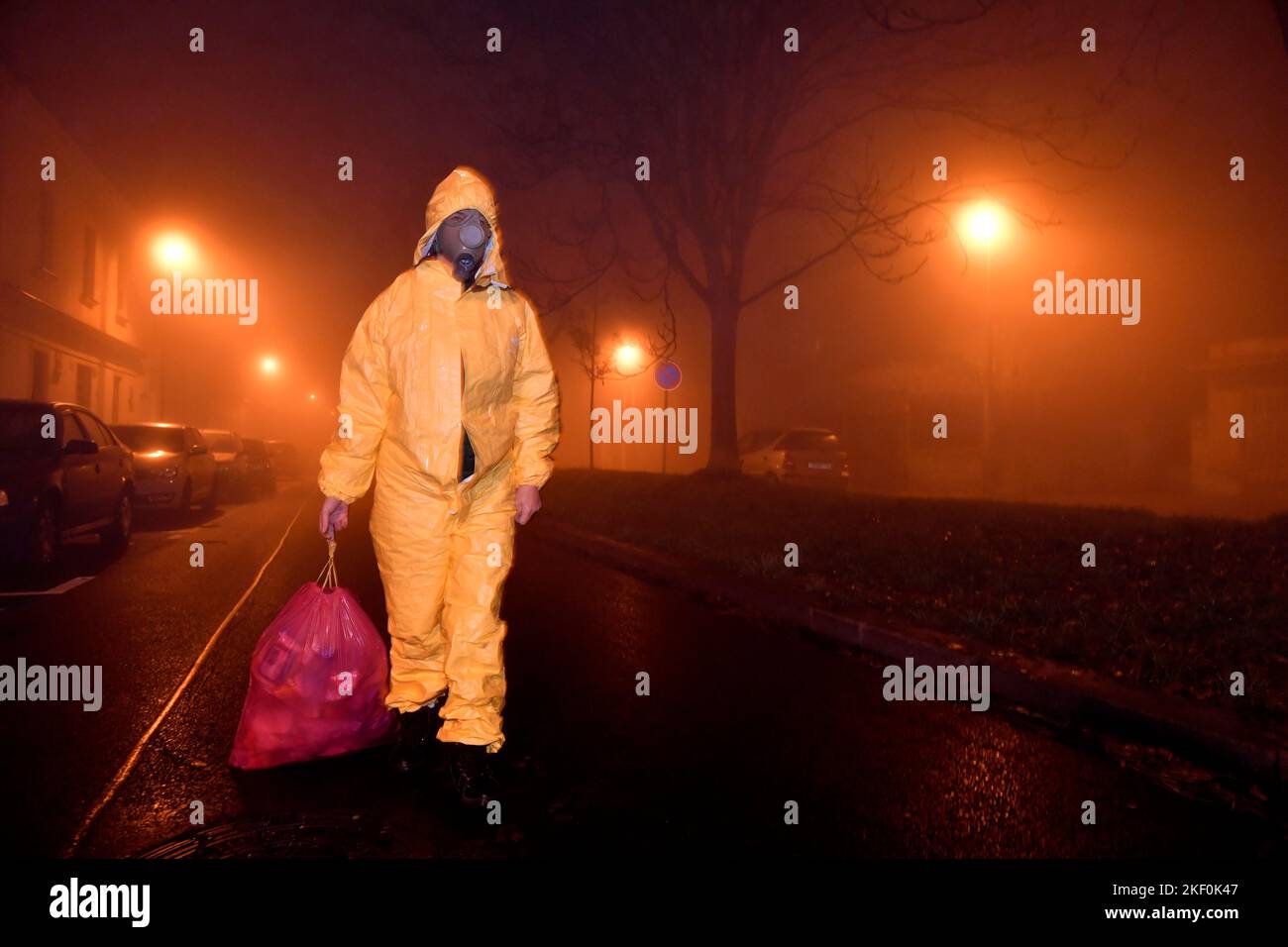 Eine Person in gelber Farbe, die auf der nächtlichen, rauchigen Straße mit einem Müllsack unterwegs ist Stockfoto