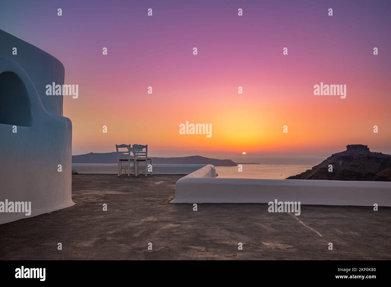 Weiße Architektur auf der Insel Santorin, Griechenland. Restaurant im Freien unter einer fantastischen Sonnenuntergangslandschaft, Stühle für Paare. Romantischer Blick auf den Sonnenuntergang, orange Stockfoto