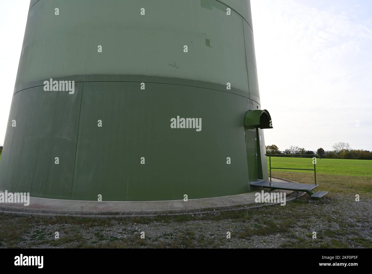 Blick auf die grüne Basis der runden Säule mit Tür einer Onshore-Windturbine, die den Bedarf der Einwohner mit erneuerbarer Energie versorgt. Stockfoto