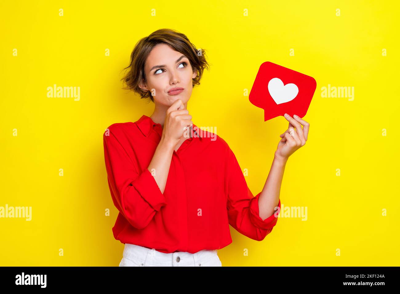 Foto von schönen liebenswert schöne positive Frau gekleidet roten Hemd aussehen leeren Raum Finger auf Kinn isoliert auf gelbem Hintergrund Stockfoto