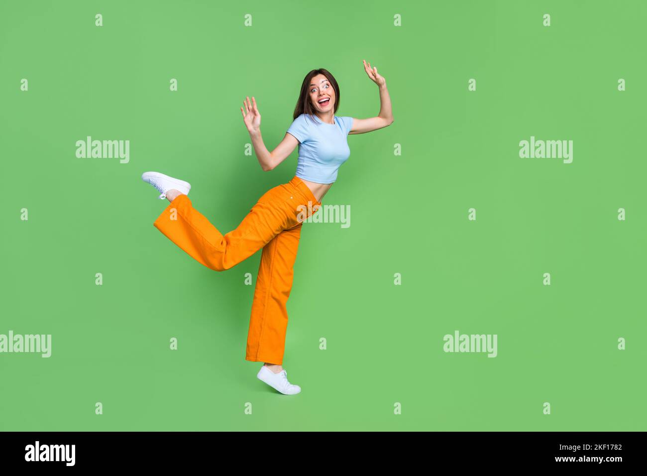 In voller Länge Profilfoto von zufrieden überglücklich Person stehend ein Bein heben Hände isoliert auf grünem Hintergrund Stockfoto