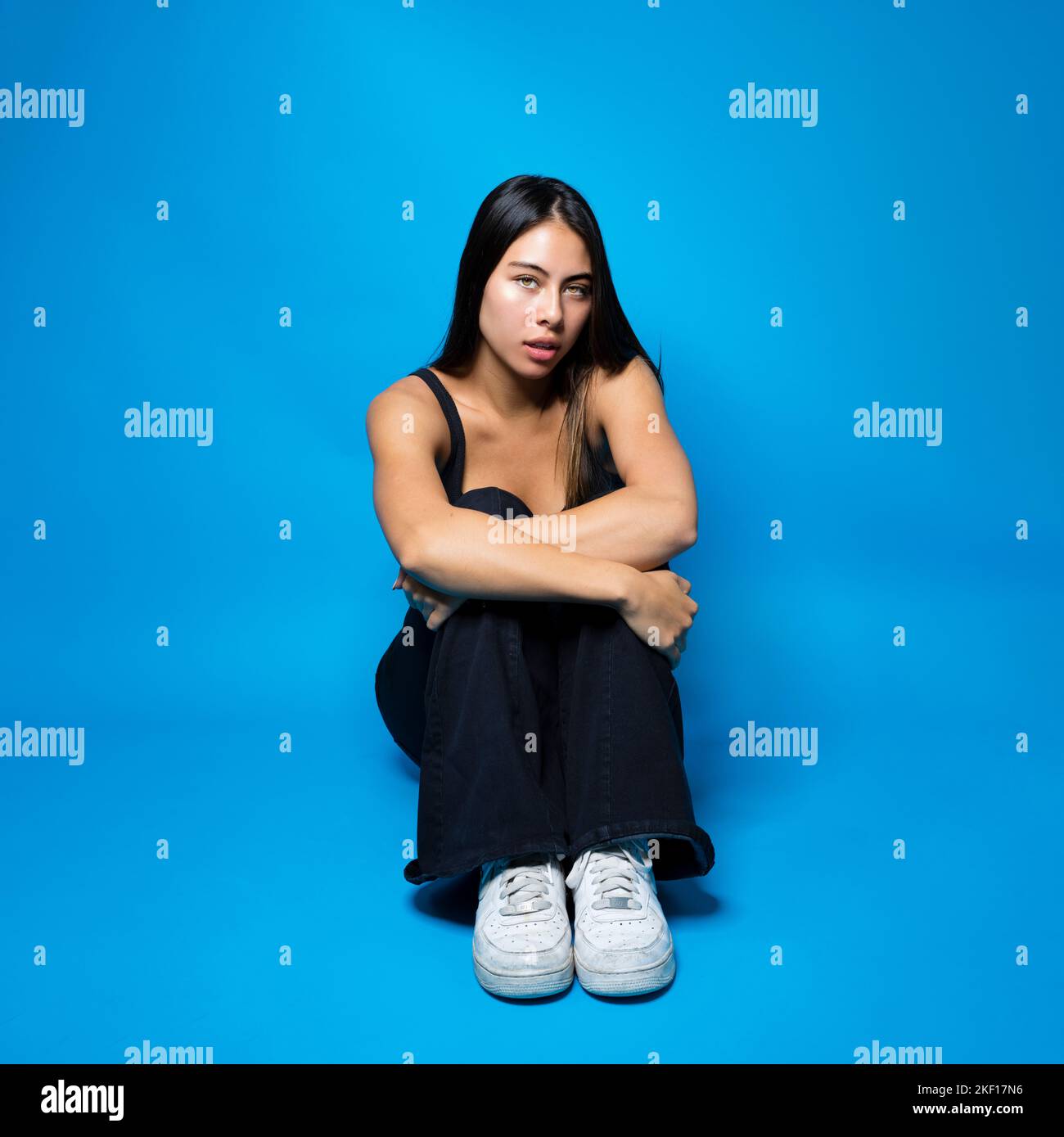 Multirassischer Teenager, der auf dem Boden in Fetalposition auf blauem Hintergrund mit Kopierraum sitzt Stockfoto