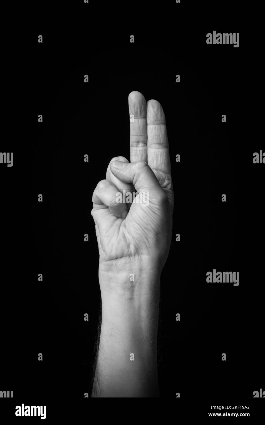 Dramatisches Schwarz-Weiß-Bild einer männlichen Hand, die den arabischen Zeichenbuchstabe „ت“ oder „TA“ mit Fingerschrift vor einem dunklen Hintergrund einschreibt. Stockfoto