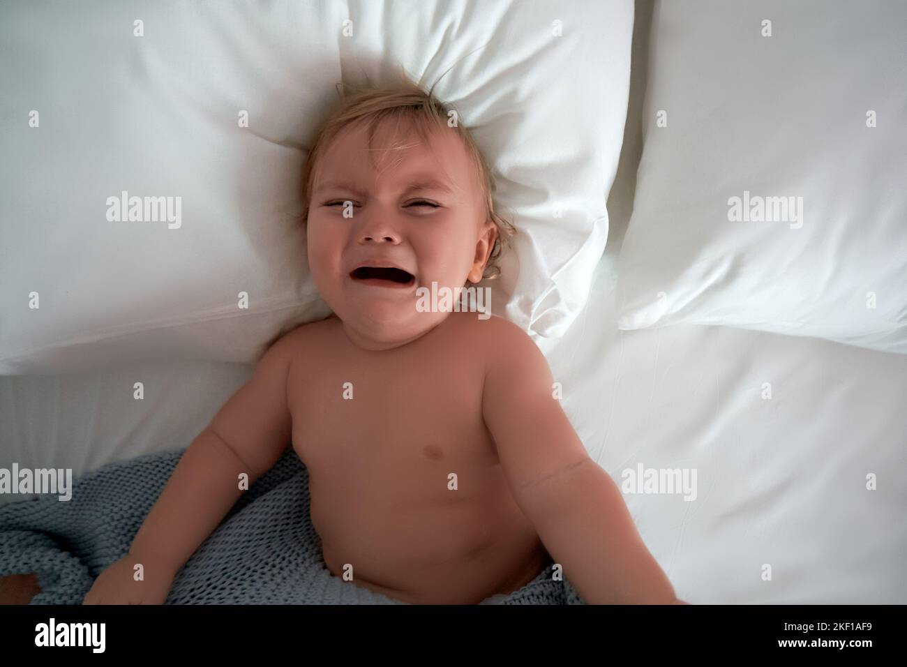 Charmantes niedliches Baby weint auf dem Bett liegend. Flach liegend. Weißer Hintergrund, Kopierbereich. Weißer Hintergrund, Kopierbereich. Stockfoto