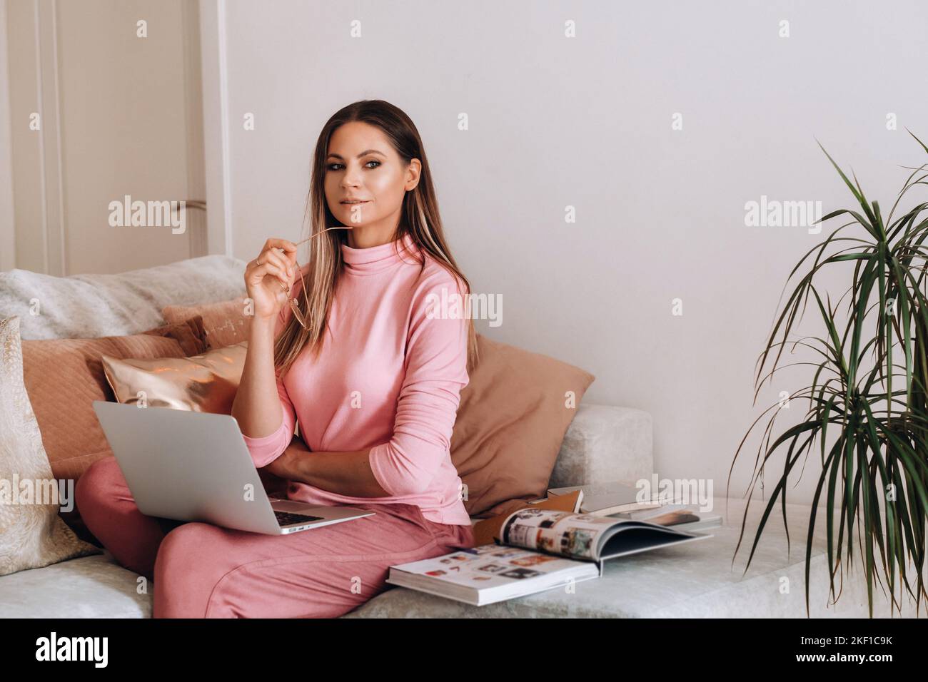 Ein Mädchen am Morgen in Schlafanzug und Brille zu Hause arbeitet auf einem Laptop, ein Mädchen isoliert sich zu Hause, ruht sich auf der Couch aus und schaut einem Laptop zu Stockfoto