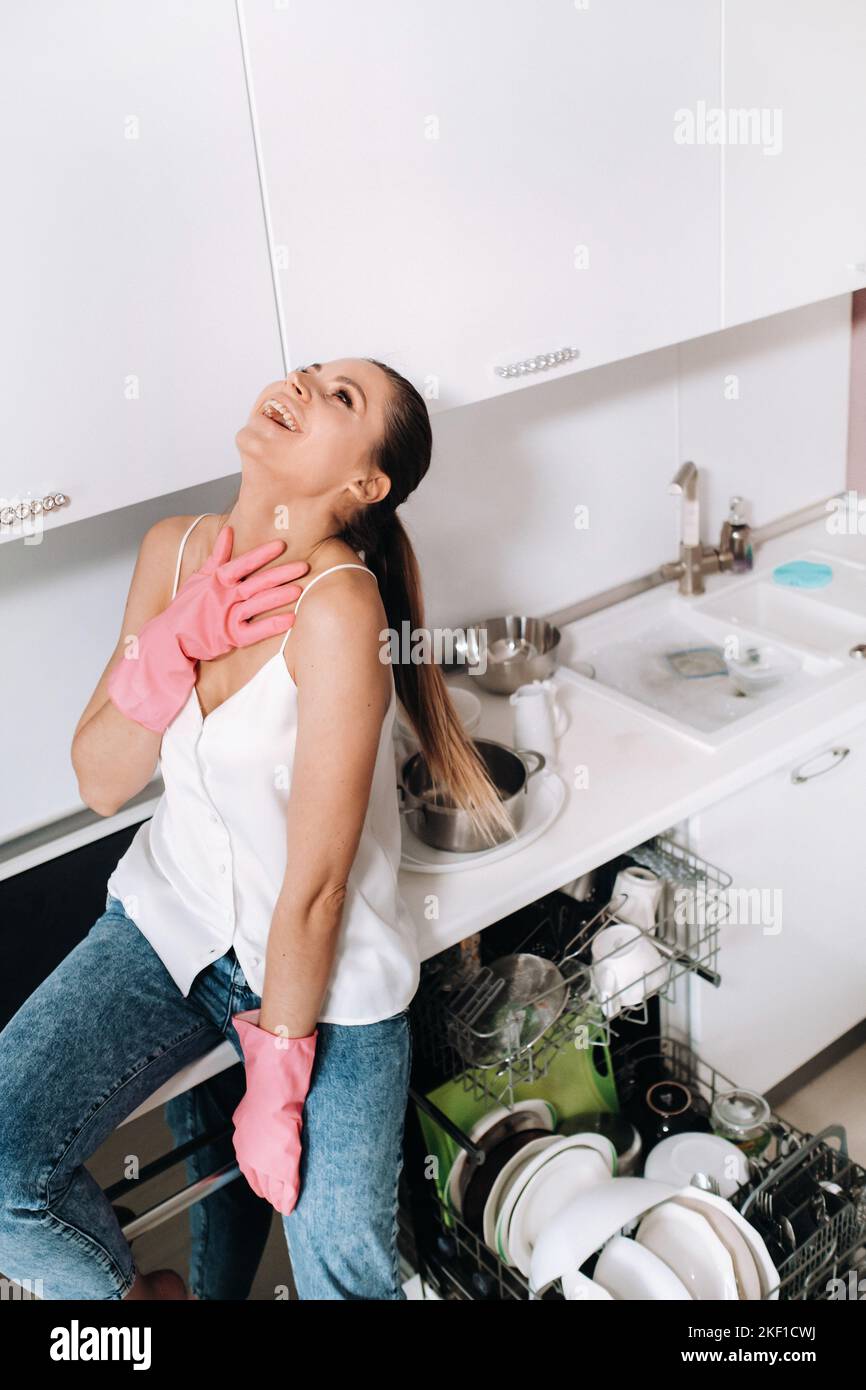 Hausfrau Mädchen in rosa Handschuhe nach der Reinigung des Hauses ist emotional und müde in der weißen Küche, das Mädchen hat das Geschirr gewaschen und ruht und Stockfoto