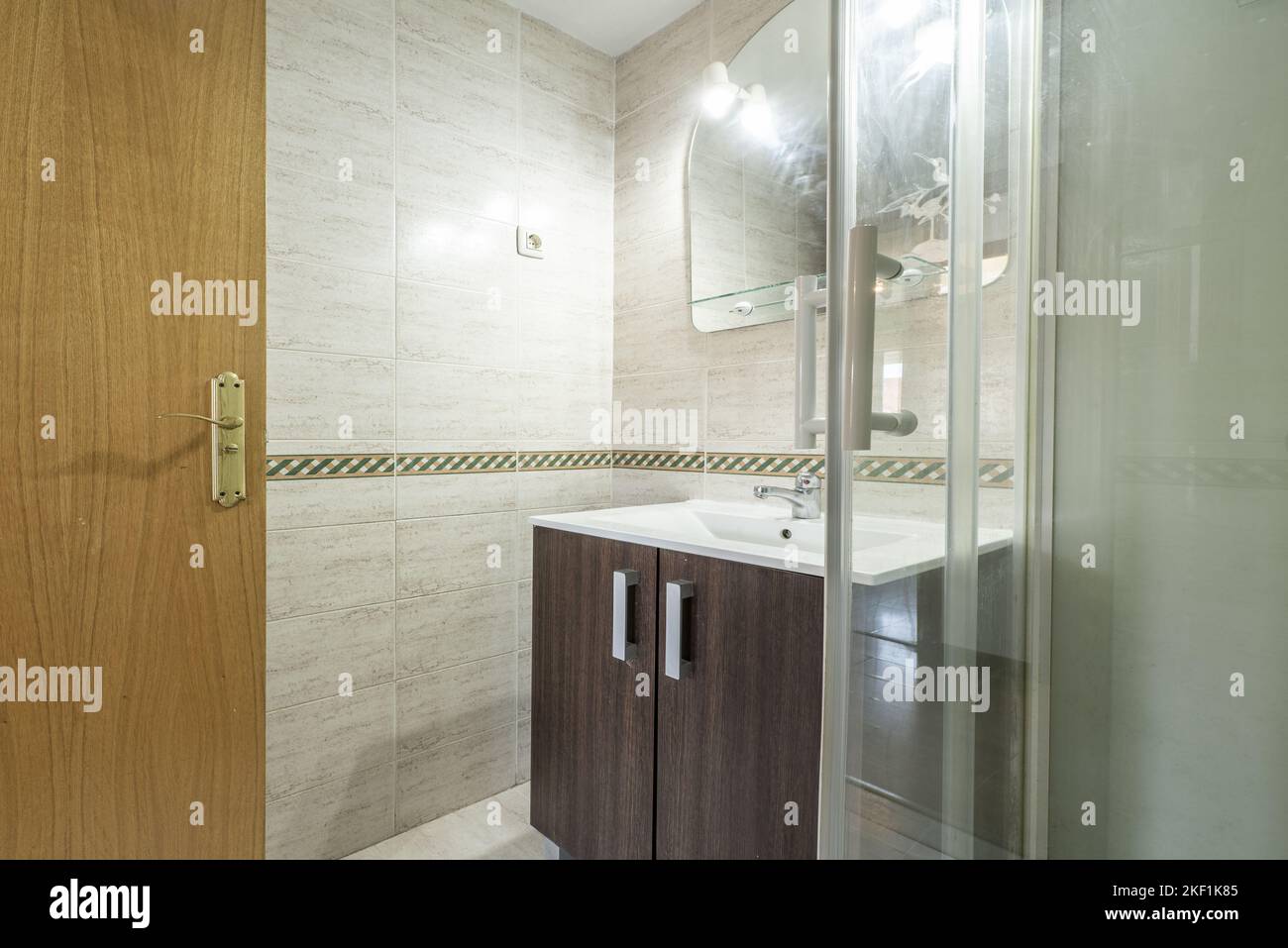 Badezimmer mit dunklen Holzmöbeln, rahmenlosem Spiegel mit Lampen und Duschkabine aus Glas Stockfoto