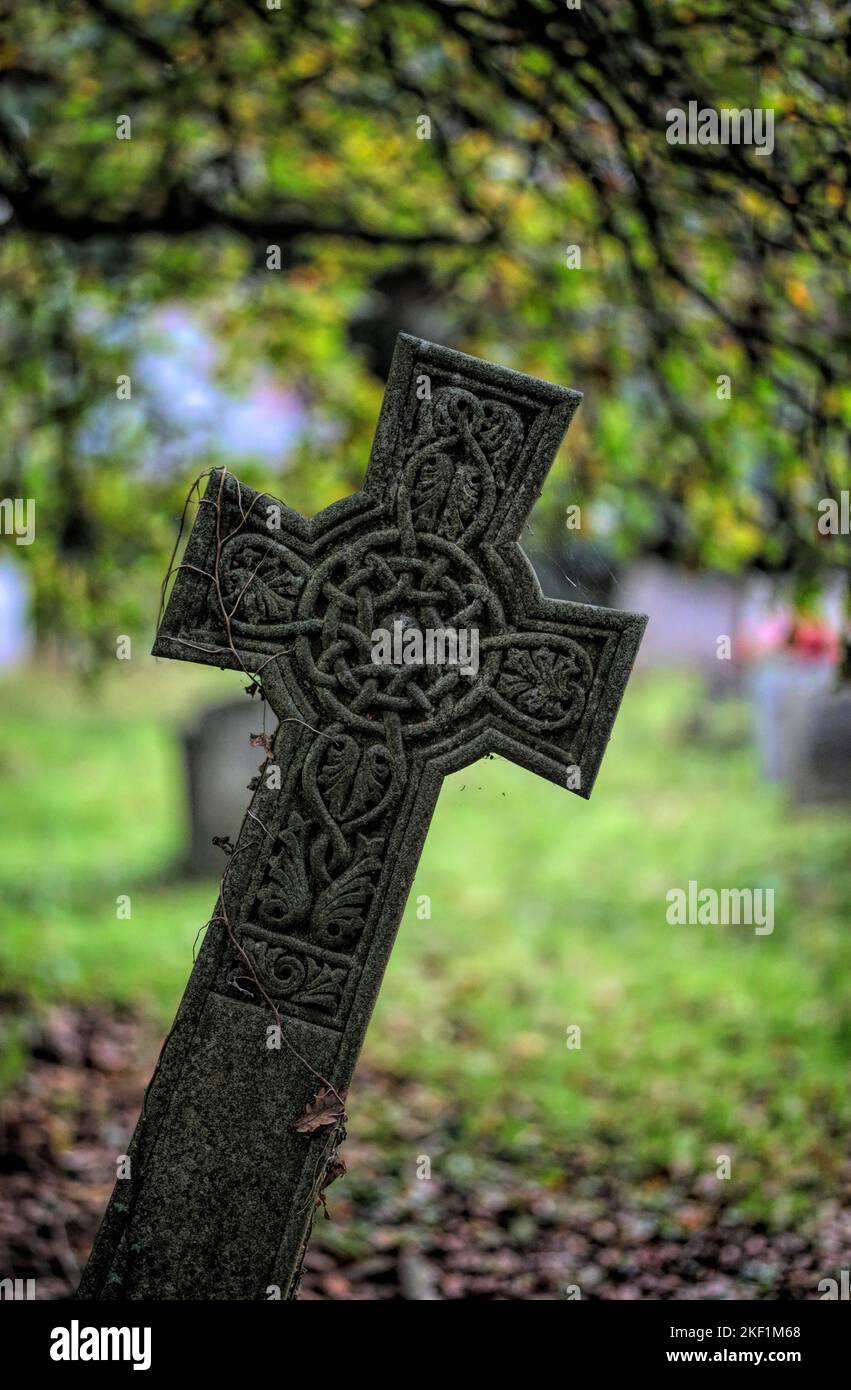 Eine vertikale Aufnahme eines Kreuzgrabsteins auf einem von Grün bedeckten Friedhof mit verschwommenem Hintergrund Stockfoto