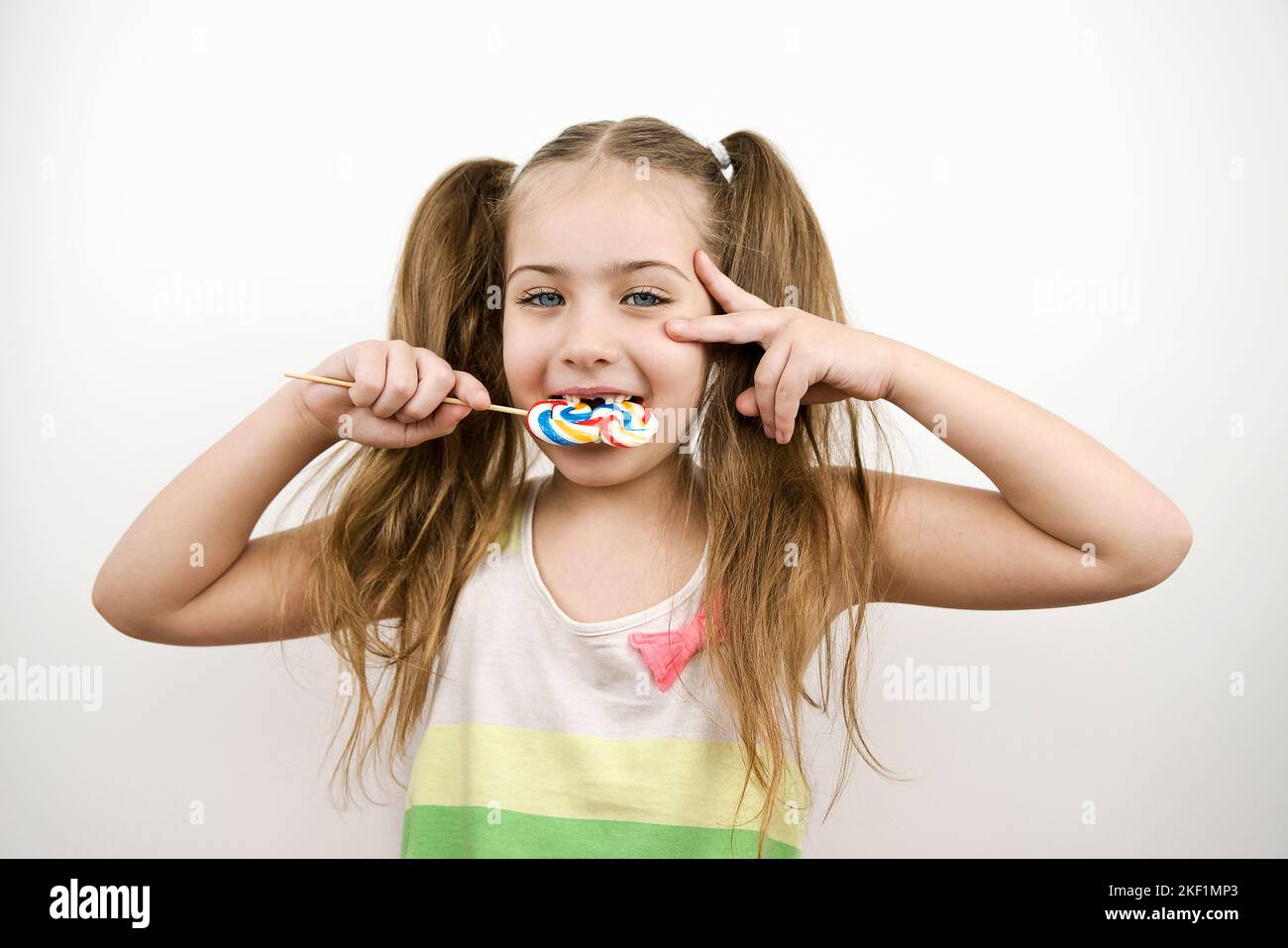 Niedliches zahnloses kleines Mädchen mit blauen Augen, das Lollipop isst. Isoliert auf Weiß Stockfoto