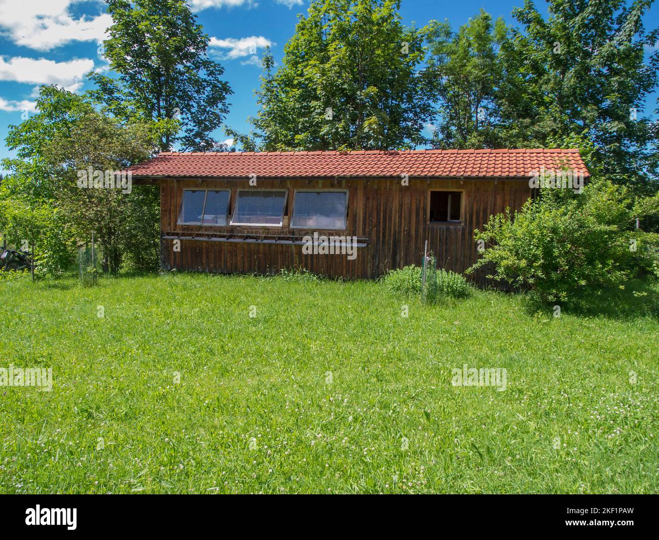 Frontansicht der langen Seite mit drei Glasfenstern eines Imkerhauses in Bayern auf einer grünen Wiese mit einer Baumgruppe im Hintergrund darunter Stockfoto
