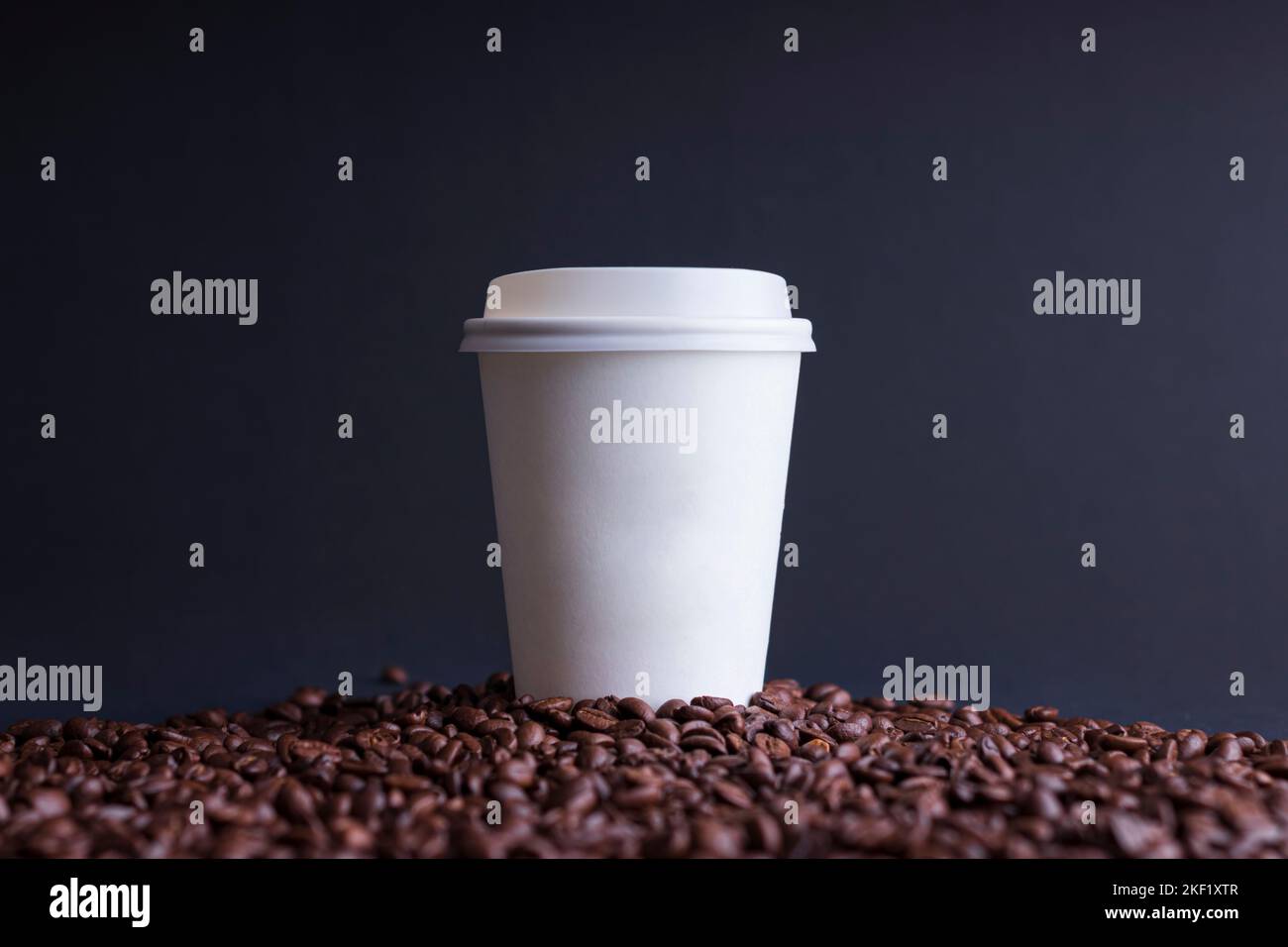Papierkaffeetasse zwischen gerösteten Kaffeebohnen, auf schwarzem Hintergrund Stockfoto