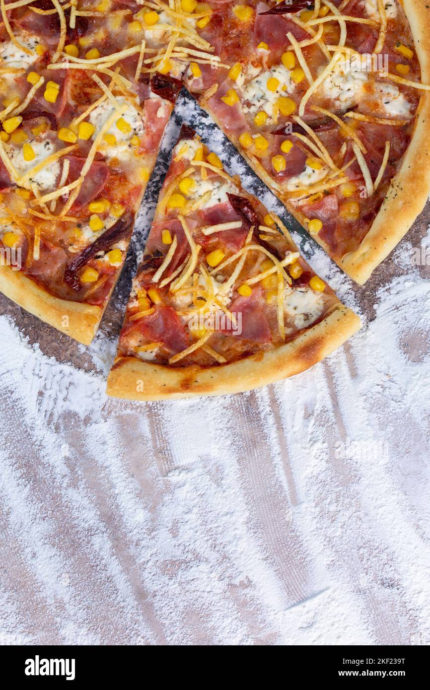 Draufsicht Pizza mit Schinken und Mais auf dem Hintergrund von Mehl. Stockfoto