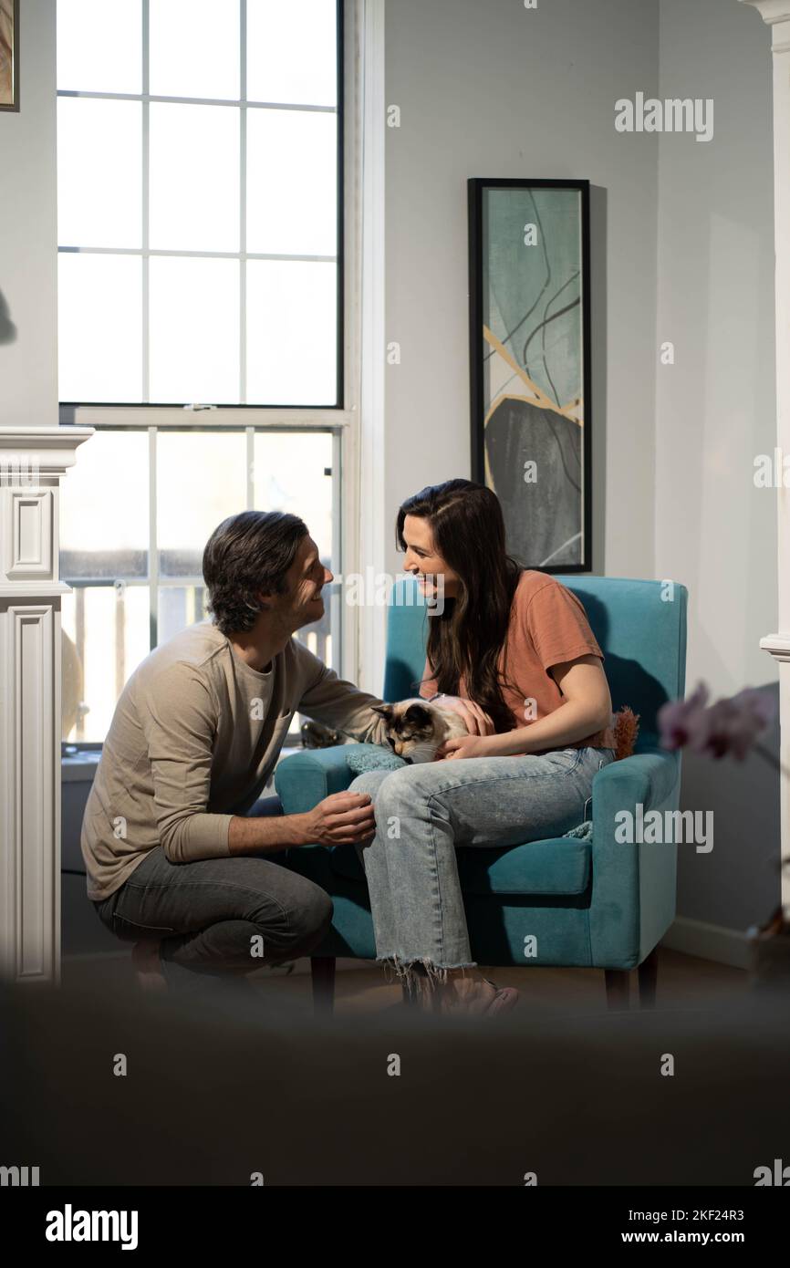 Ein Mann und eine Frau im Wohnzimmer mit ihrer Katze, die sich liebevoll in einem blauen Stuhl anschmiegen. Stockfoto