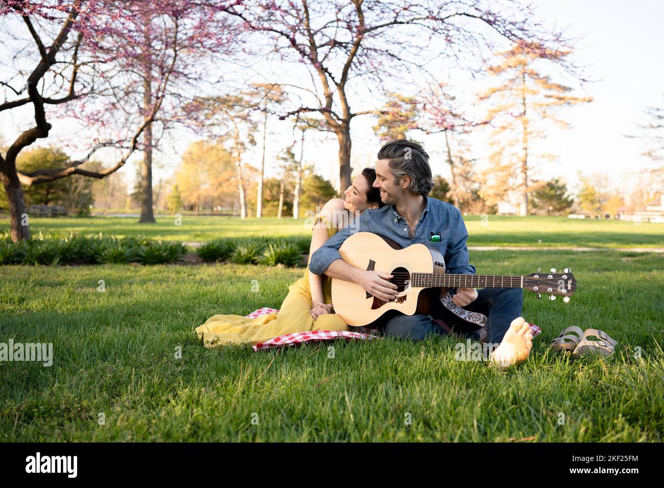 Verliebte Paare bei einem Picknick im Forest Park. Der Mann spielt eine Gitarre für seine Frau. Stockfoto