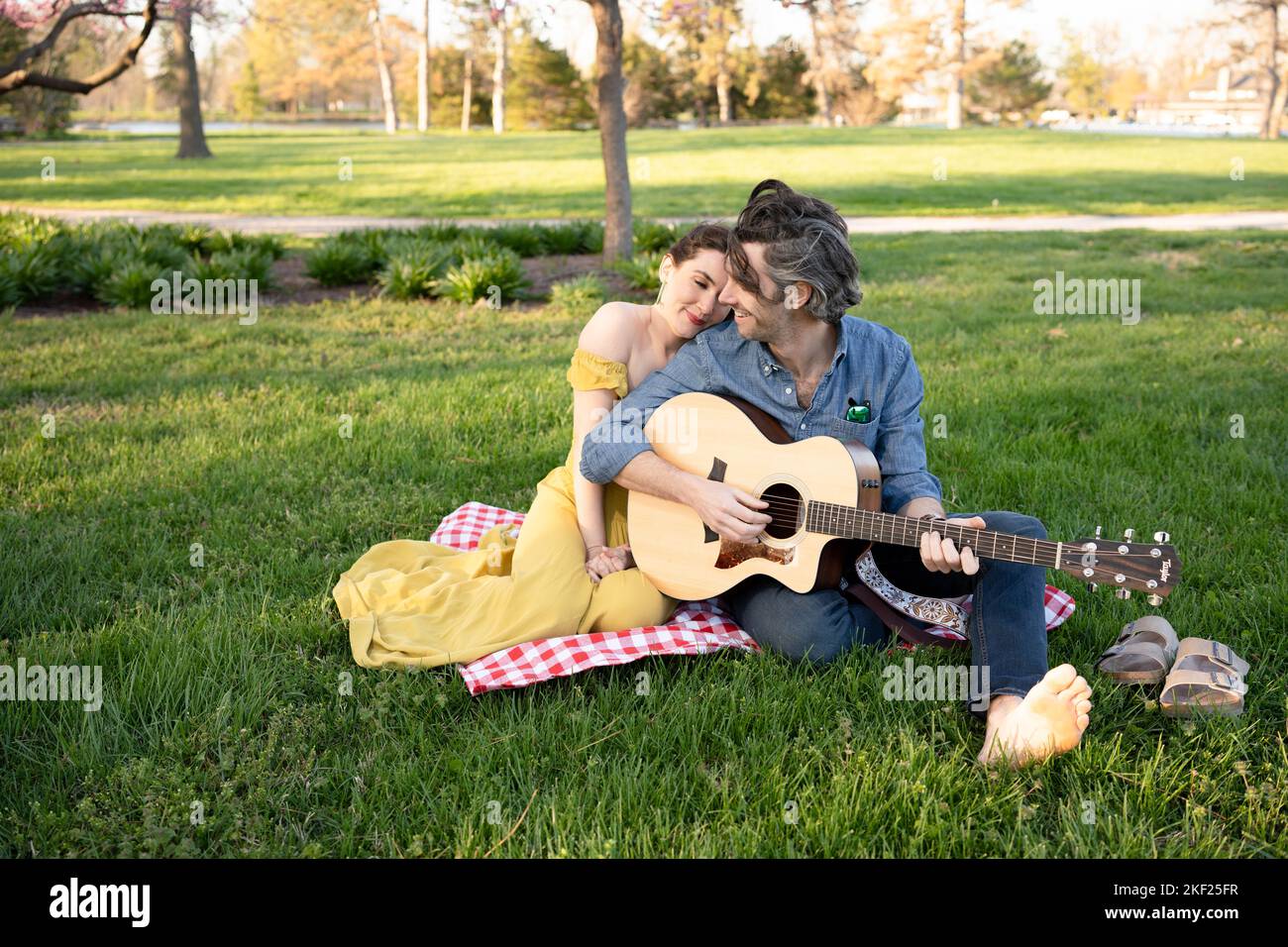 Verliebte Paare bei einem Picknick im Forest Park. Der Mann spielt eine Gitarre für seine Frau. Stockfoto