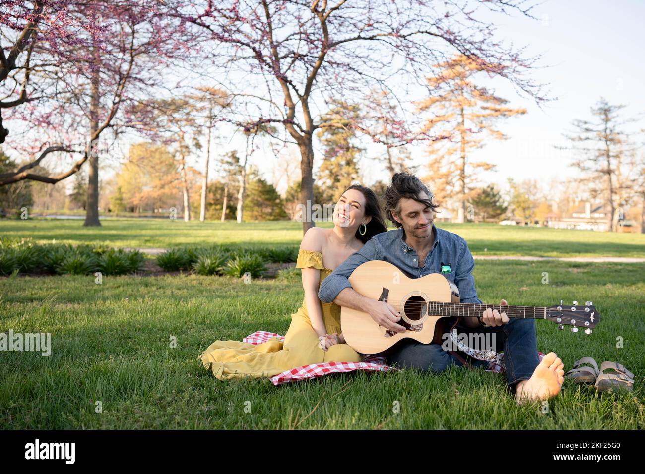 Verliebte Paare bei einem Picknick im Forest Park. Der Mann spielt eine Gitarre für seine Frau. Stockfoto