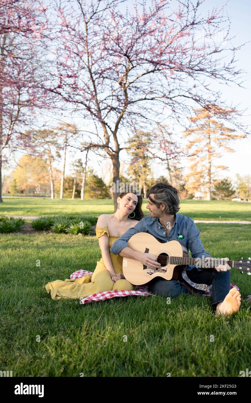 Verliebte Paare bei einem Picknick im Forest Park. Der Mann spielt eine Gitarre für seine Frau. Stockfoto