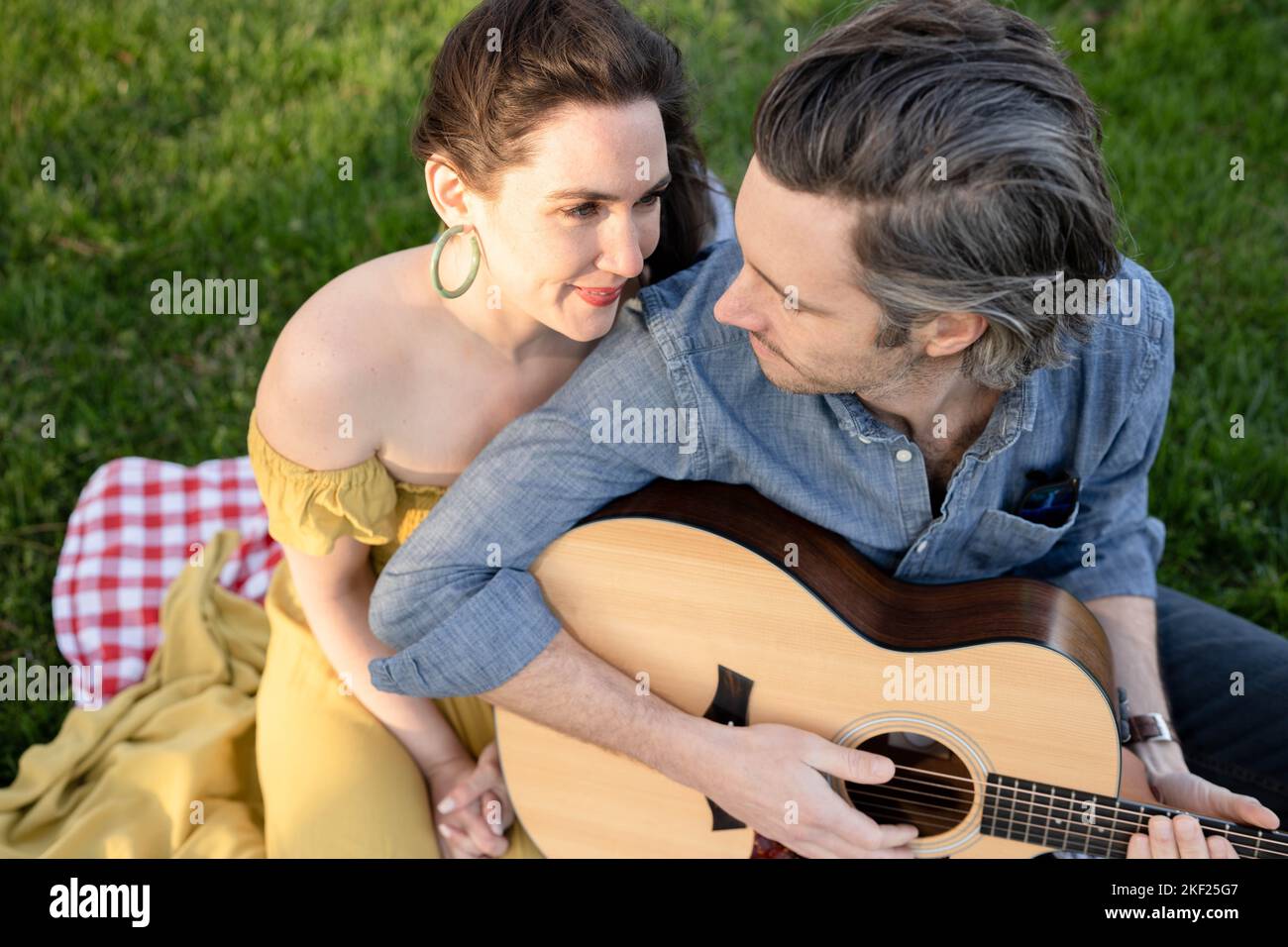 Verliebte Paare bei einem Picknick im Forest Park. Der Mann spielt eine Gitarre für seine Frau. Stockfoto