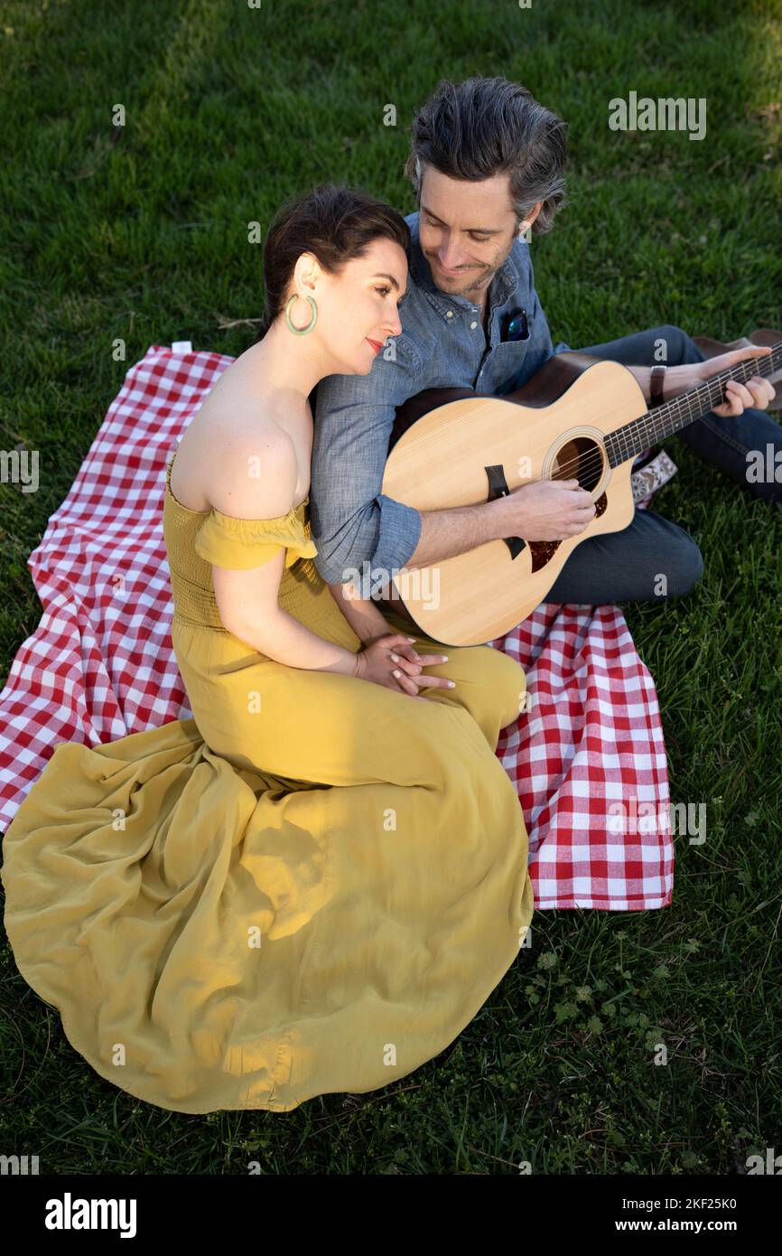 Verliebte Paare bei einem Picknick im Forest Park. Der Mann spielt eine Gitarre für seine Frau. Stockfoto
