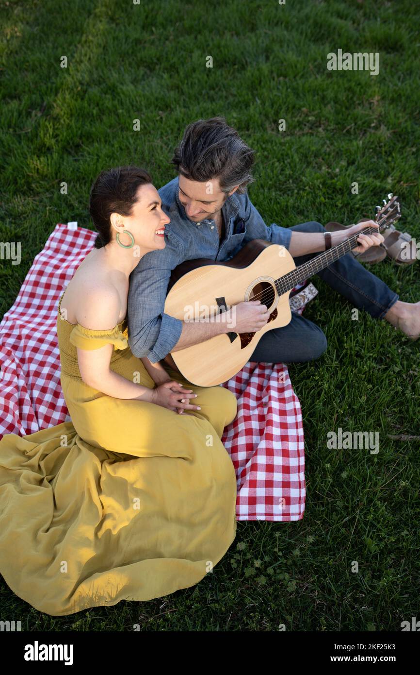 Verliebte Paare bei einem Picknick im Forest Park. Der Mann spielt eine Gitarre für seine Frau. Stockfoto