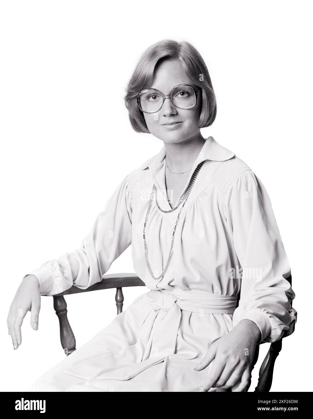 1970S FRAU SITZT IN HOLZSTUHL TRAGEN GÜRTEL KLEID KETTE HALSKETTE GROSSE BRILLE SEITE JUNGE FRISUR BLICK AUF KAMERA - G8392 HAR001 HARS PERSONEN DURCHDACHT BERUF VERTRAUEN FÜHRUNGSKRÄFTE BRILLEN B&W GESCHÄFTSFRAU BLICKKONTAKT BERUF KARRIERE FRISUR LEHRER STOLZ SUPERVISOR BERUFE CHEFS VERBINDUNGSSEITE ERZIEHER STILVOLLE GESCHÄFTSFRAUEN AUFRICHTIG BELTED FEIERLICHE AUSBILDUNG PÄDAGOGEN FOKUSSIERTE AUSBILDER INTENSIVE MANAGER MID-ADULT MID-ADULT FRAU SCHULE LEHRT SCHWARZ UND WEISS SORGFÄLTIGE KAUKASISCHE ETHNIE ERNST HAR001 ABSICHT ALTMODISCH Stockfoto