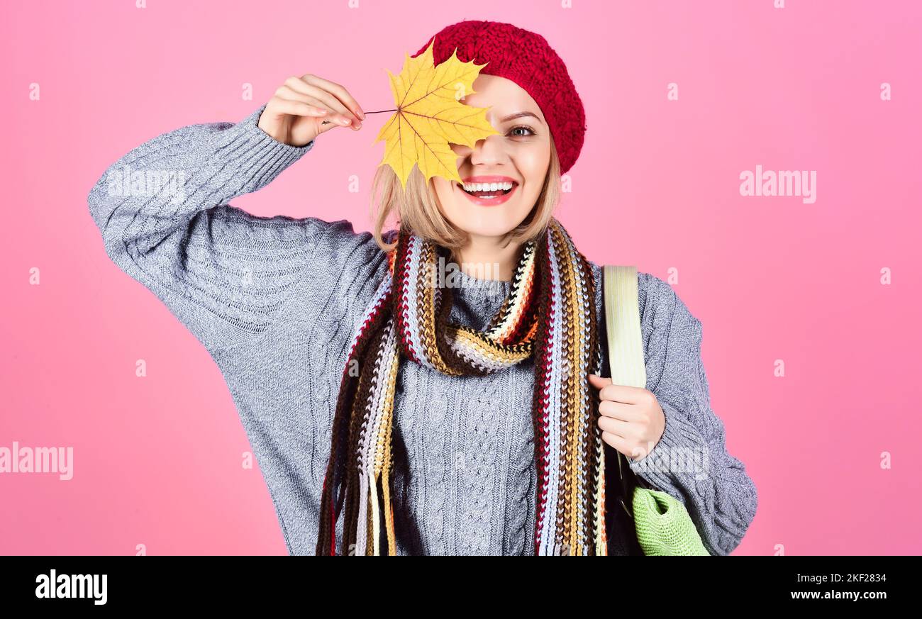 Lächelndes Mädchen versteckt Auge durch gelbes Ahornblatt. Frau in warmer Kleidung mit Einkaufstasche. Saisonangebot. Stockfoto