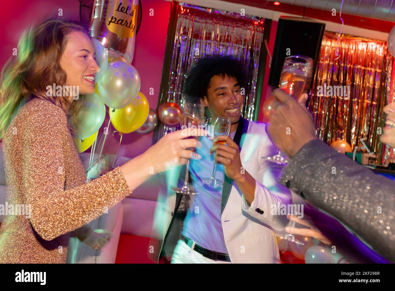 Drei glückliche, vielfältige männliche und weibliche Freunde, die mit einem Glas Champagner im Nachtclub anstoßen Stockfoto