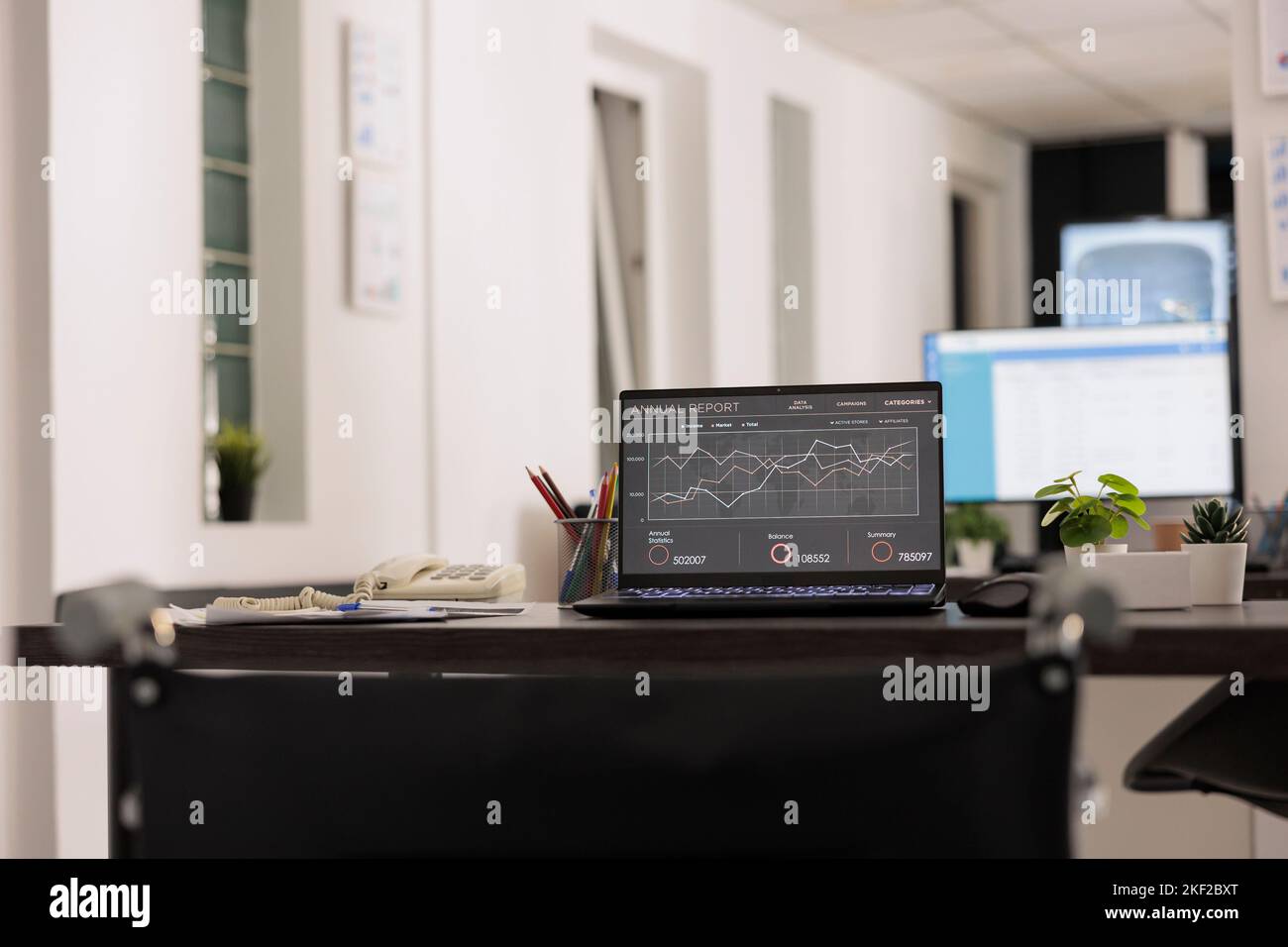 Arbeitsplatz mit tragbarem Computer, Gerät und einigen Papieren auf dem Tisch ohne Menschen in einem modernen Coworking-Büro. Anzeige mit jährlichem Statistikbericht am unbemannten Arbeitsplatz. Stockfoto